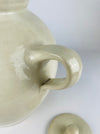 Antique French cruche pot displaying the applied pouring spout, twin loop handles and broad neck that distinguish this regional household vessel. An old hairline follows part of the spout attachment with localized glaze loss, while the surrounding cream terracotta surface retains natural throwing marks and patina.
