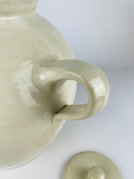 Antique French cruche pot displaying the applied pouring spout, twin loop handles and broad neck that distinguish this regional household vessel. An old hairline follows part of the spout attachment with localized glaze loss, while the surrounding cream terracotta surface retains natural throwing marks and patina.