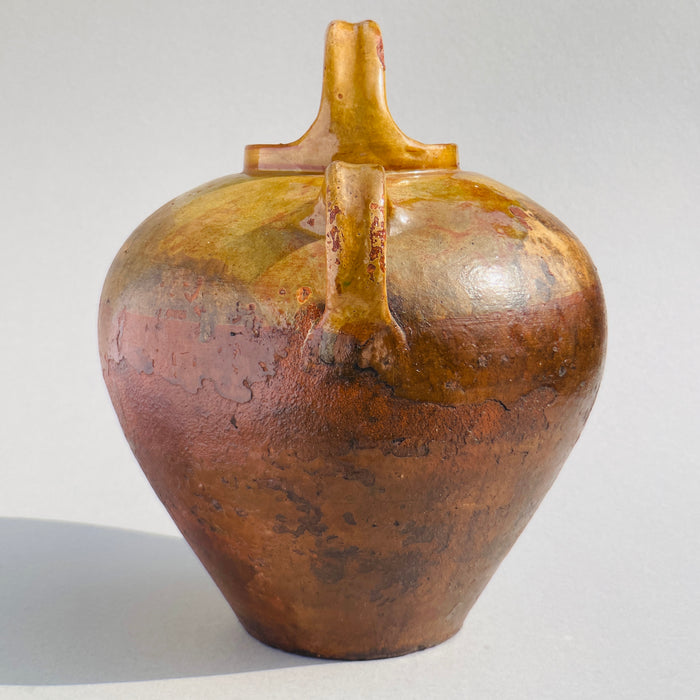 Side angle highlighting the wide body tapering down to a narrow foot with a smooth clay texture and ochre glaze variations.