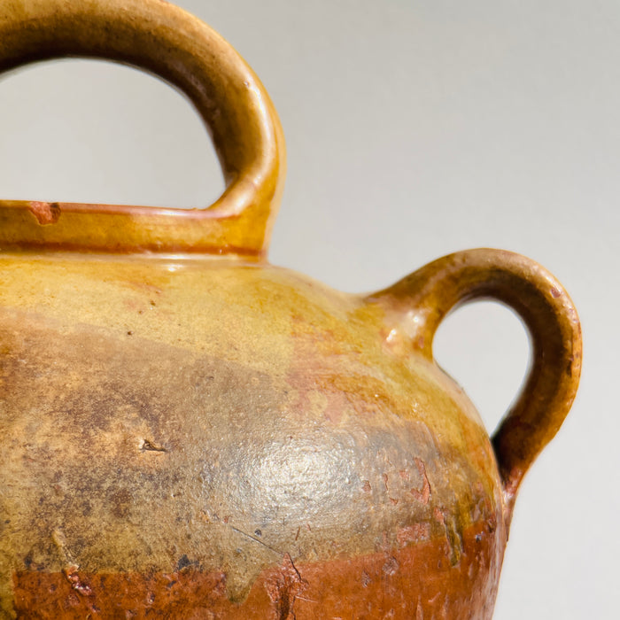 Side angle highlighting the wide body tapering down to a narrow foot with a smooth clay texture and ochre glaze variations.