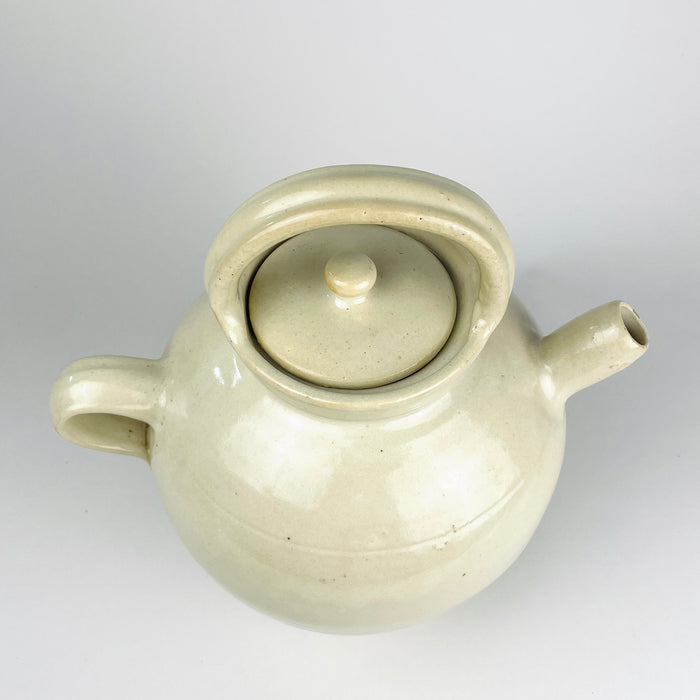 Early 1900s French cruche pot formed on a potter’s wheel from fired clay and covered in an irregular cream glaze. The broad cylindrical neck, symmetrical loop handles and small projecting spout identify its traditional household vessel form, while its generous scale gives this antique pottery strong decorative presence.