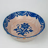 Ceramic bowl with blue floral design on a white background. Spanish terracotta wabi-sabi bowl with opaque tin glaze and cobalt blue floral motif, shaped as a traditional lebrillo serving bowl and displayed as wall hanging ceramic decor using the attached wire on the back. The border shows layered wave brushwork. Notable rim chips and glaze losses are present, consistent with age. Ideal for vintage kitchen styling and Mediterranean decor.