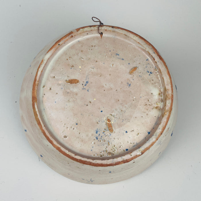 Spanish Fajalauza lebrillo bowl from Granada in tin glazed terracotta, painted in cobalt blue with a stylized flower, leaves, and small dotted accents in the center. The inner rim shows repeating blue wave bands with teardrop motifs. A wire hanger is attached on the reverse for wall display as Mediterranean decor.