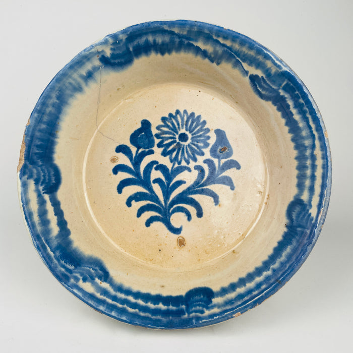 Blue and white Spanish decorative bowl in a traditional lebrillo form, featuring a hand-painted cobalt floral sprig with radiating petals and leaf scrolls. The wide rim band is painted in cobalt with soft transitions typical of brushed pigment on glaze. Ideal for Mediterranean decor dining, vintage kitchen display, and ceramic wall decor collections.