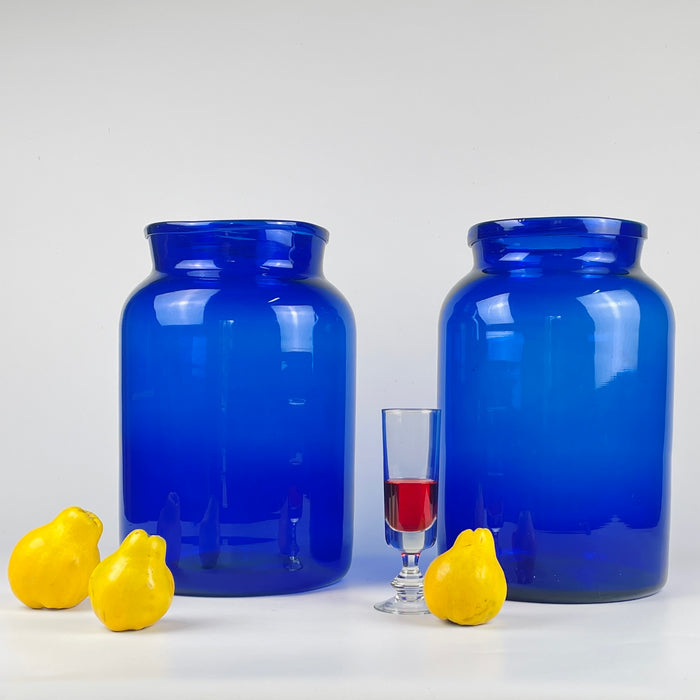 Pair of antique French cobalt blue glass vases or apothecary jars, hand blown in the 19th century, with intense deep blue pigmentation created using cobalt oxide minerals. The tall cylindrical forms exhibit natural air bubbles, subtle surface variations, and thickness differences around the mouth, confirming historic hand shaping. These vases suit French country decor, Mediterranean decor, organic modern decor, and rustic farmhouse styling, serving as bold sculptural accents.