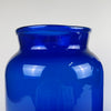 Cobalt blue glass, placed on a neutral surface to enhance the intensity of the blue colour. The thick glass construction suggests apothecary or chemical storage origins from the late 1800s. Their vertical form and saturated colour integrate well with coastal modern decor, Mediterranean decor, and rustic contemporary spaces.