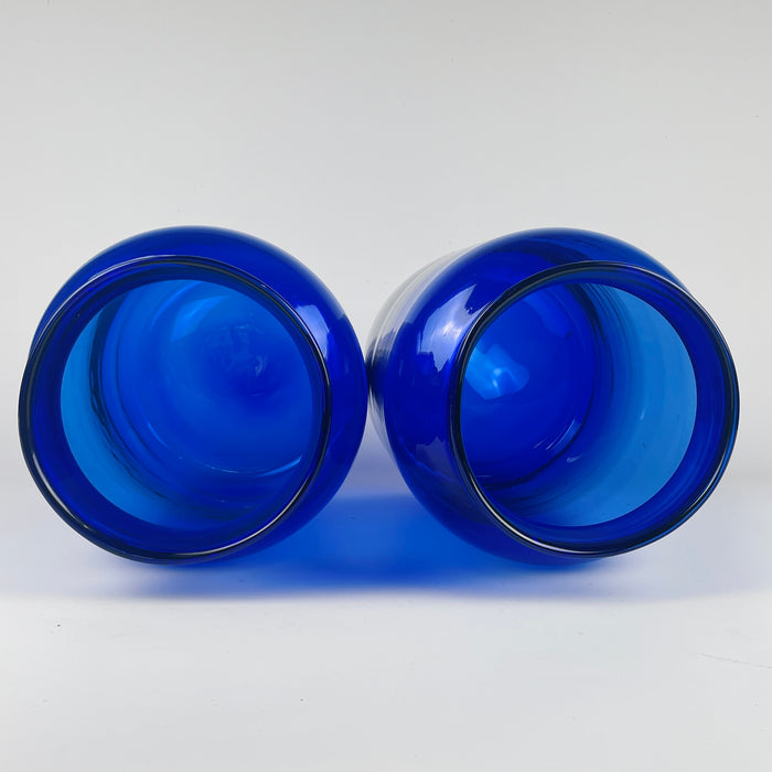 Side-by-side image of both antique cobalt blue vases, showing their tall silhouettes, heavy glass walls, and deep blue tones used historically to protect apothecary contents from light. The pair’s hand blown characteristics—subtle asymmetry, trapped bubbles, and mouth variation—are visible. Suitable for organic modern decor, French country decor, or as sculptural focal points in entryways or living rooms.