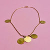 Hammered coin disc chain necklace in gold-tone alloy. Features five golden discs with textured surfaces on a fine link chain. Designed as artisan jewelry, ideal for summer fashion, Mediterranean jewelry styling, and minimalist layering jewelry collections.
