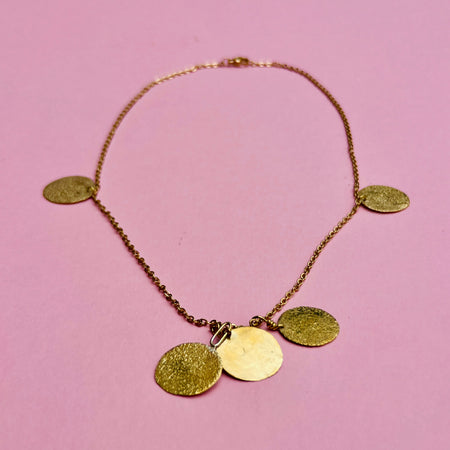 Hammered coin disc chain necklace in gold-tone alloy. Features five golden discs with textured surfaces on a fine link chain. Designed as artisan jewelry, ideal for summer fashion, Mediterranean jewelry styling, and minimalist layering jewelry collections.