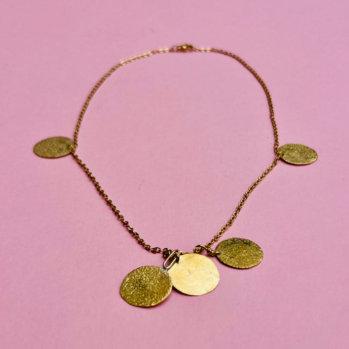 Hammered coin disc chain necklace in gold-tone alloy. Features five golden discs with textured surfaces on a fine link chain. Designed as artisan jewelry, ideal for summer fashion, Mediterranean jewelry styling, and minimalist layering jewelry collections.