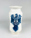 Large Antique Spanish Talavera albarello apothecary jar in glossy white glazed earthenware, decorated with a cobalt blue heraldic eagle carrying a shield with a cross and vertical stripes. The tall wheel thrown vessel has rounded shoulders, gently waisted sides, a flared rim and a circular foot. The decorative pharmacy jar is a distinctive example of Spanish blue and white pottery.