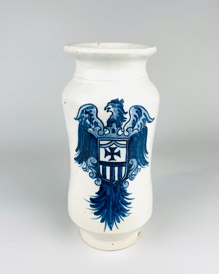 Large Antique Spanish Talavera albarello apothecary jar in glossy white glazed earthenware, decorated with a cobalt blue heraldic eagle carrying a shield with a cross and vertical stripes. The tall wheel thrown vessel has rounded shoulders, gently waisted sides, a flared rim and a circular foot. The decorative pharmacy jar is a distinctive example of Spanish blue and white pottery.