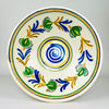 Antique Spanish lebrillo bowl in glazed earthenware, dating to the early 20th century and decorated in the Castilian remolino tradition. A cobalt blue spiral fills the centre while green vegetal forms, honey yellow branches and black accents rotate across the cream ground. The shallow flared basin works as ceramic wall art or a decorative bowl.