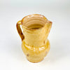 Small antique Spanish terracotta jug weighing 500 g, with a rounded belly and tall cylindrical neck balanced by a narrow circular foot. The yellow ceramic glaze shows natural tonal variation and substantial wear, while the pinched lip and sturdy handle identify the piece as a traditional liquid pitcher now suited to decorative farmhouse display.