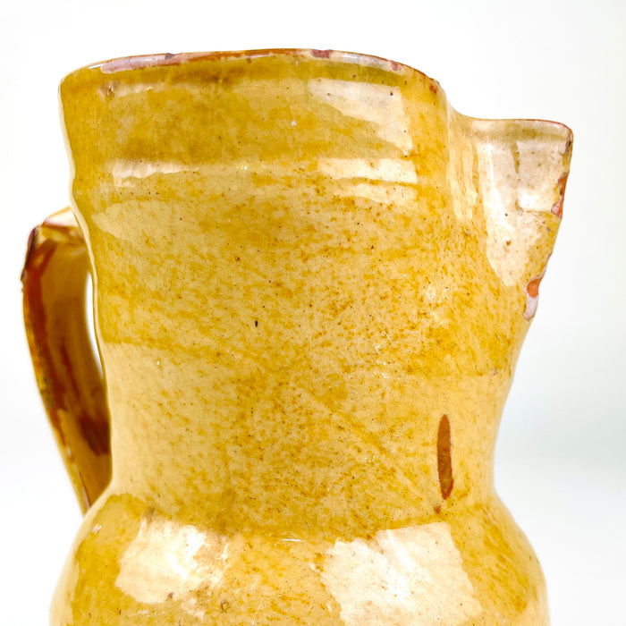 Antique yellow pottery pitcher from Spain with a glossy ochre and honey-toned glaze, visible turning rings and an individually shaped spout. The 19th century earthenware vessel retains glaze losses, rim chips, crazing and exposed red terracotta, creating authentic patina for Mediterranean decor, farmhouse decor or wabi sabi decor.