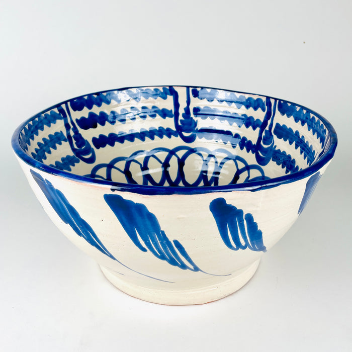 Hand painted exterior of the Spanish Fajalauza lebrillo bowl with sweeping cobalt marks extending across the cream glazed earthenware body. Small pinholes, glaze variations and subtle forming lines remain visible beneath the finish, documenting the artisan production of this large Los Arrayanes bowl from Granada.