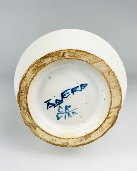 Underside of a vintage Spanish Talavera style albarello jar showing a handwritten cobalt blue inscription and secondary painter's monogram inside the recessed circular base. The surrounding foot ring exposes buff-coloured pottery with surface wear and residue. These visible markings and construction details are important identifying characteristics of this hand decorated ceramic apothecary vessel.