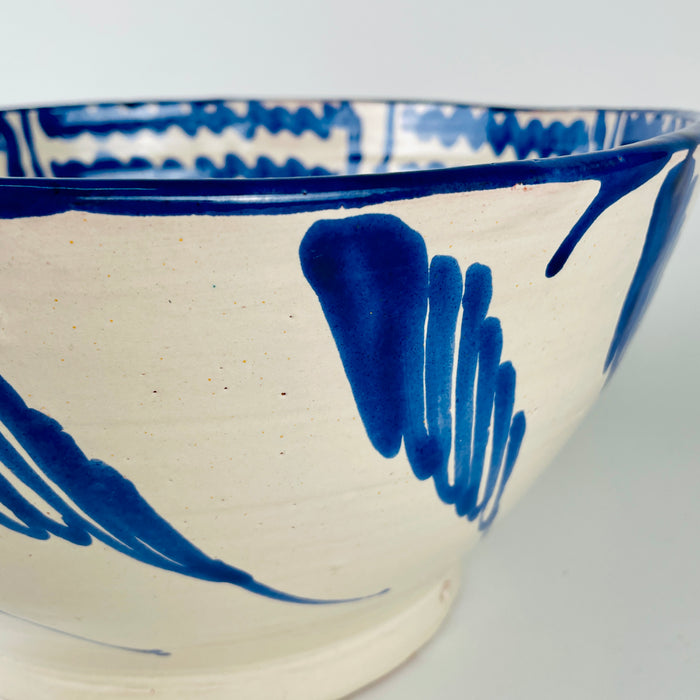 Large Fajalauza bowl held to display the full cobalt blue interior pattern and generous 33 cm diameter. The Cerámica Los Arrayanes earthenware piece features a central flower, looping geometric border and concentric scalloped lines on a cream glaze, demonstrating its scale as Spanish ceramic wall art, serving ware or a table centerpiece.