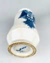 Spanish blue and white Talavera albarello resting to reveal its circular foot, recessed underside and cobalt blue painted base markings. The white glazed ceramic body carries part of the heraldic eagle and striped shield decoration, while the foot ring shows exposed earthenware and small irregularities. The base inscription and distinctive waisted form contribute to the identity of this vintage pharmacy-style jar.