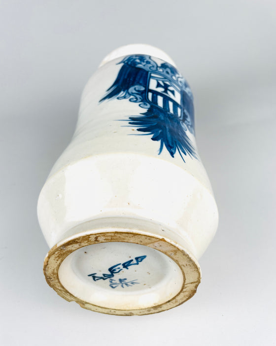 Spanish blue and white Talavera albarello resting to reveal its circular foot, recessed underside and cobalt blue painted base markings. The white glazed ceramic body carries part of the heraldic eagle and striped shield decoration, while the foot ring shows exposed earthenware and small irregularities. The base inscription and distinctive waisted form contribute to the identity of this vintage pharmacy-style jar.