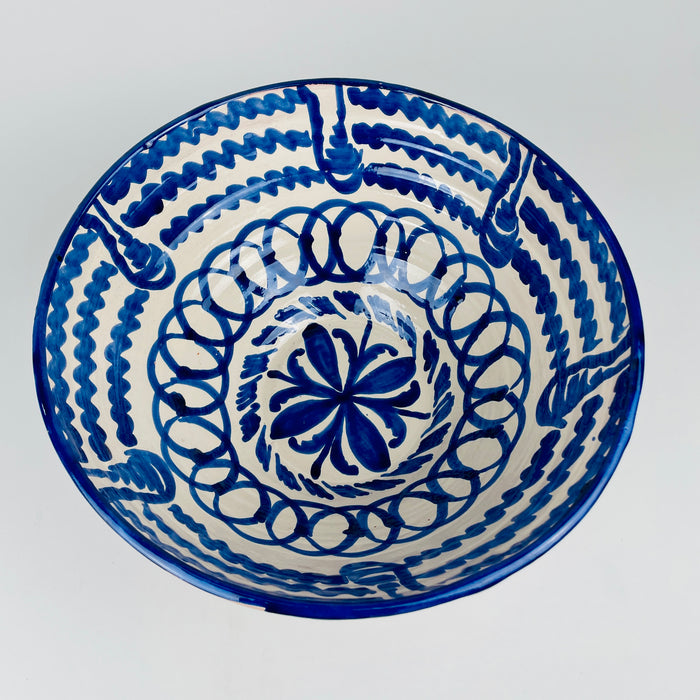Substantial Spanish Fajalauza serving bowl with a broad flared rim, deep rounded body and raised circular foot. Cobalt blue brush motifs punctuate the cream glazed exterior while the densely painted interior remains visible above the rim, showing the contrast between restrained outer decoration and elaborate Granada folk pottery ornament.