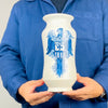 Vintage Spanish Talavera albarello made from white glazed earthenware with a large cobalt blue eagle supporting a heraldic shield. The decorative vessel has a traditionally waisted pharmacy jar shape, extended mouth and small pedestal-like foot. Its dramatic blue and white surface makes it a suitable focal point for Mediterranean decor, displayed among neutral linens and aged wooden furniture.