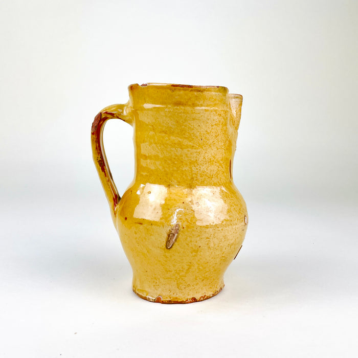 Antique Spanish yellow terracotta jug dating to the late 19th century, wheel thrown in red earthenware and finished with a warm honey glaze. The compact pitcher has a rounded belly, tall cylindrical neck, pinched pouring spout, circular foot and applied loop handle, with aged wear suited to Mediterranean decor and Spanish folk pottery collections.