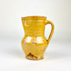 Late 19th century Spanish pottery jug formed on the wheel with a rounded body, tall neck, small foot and curved strap handle. The yellow glazed terracotta surface varies from pale cream to deep mustard, while scattered abrasions and clay exposures document long domestic use as a traditional pitcher for serving water or wine.