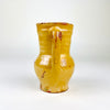 Antique Castilian pottery pitcher with a hand-shaped pouring spout and applied handle joining the shoulder to the rim. The red terracotta body is covered in a translucent honey yellow glaze that pools around the neck and handle, with extensive age-related rubbing, chips and surface crazing visible across this Spanish folk art vessel.