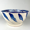 Central floral motif inside the Spanish Fajalauza lebrillo bowl, painted in deep cobalt blue and surrounded by a ring of leaflike strokes and overlapping circular ornament. The cream glazed terracotta body and confident freehand decoration identify a substantial Granada pottery serving bowl that also works as blue and white ceramic wall art.