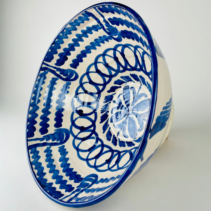 Large Los Arrayanes lebrillo bowl formed from terracotta earthenware and finished with a creamy glaze, cobalt rim and sweeping blue exterior brushstrokes. The handmade profile is slightly irregular, with a wide mouth and sturdy footed base that emphasize the scale and weight of this Granada serving bowl and decorative Spanish ceramic.