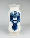 Antique Talavera style Spanish apothecary jar with a centrally placed heraldic eagle painted in deep and light cobalt blue on a creamy white ceramic ground. The eagle has extended wings, ornamental scrolls and a long feathered tail surrounding its shield. This substantial albarello vessel combines a traditional pharmacy jar silhouette with graphic historic decorative motifs.