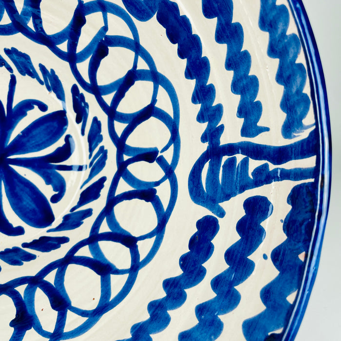 Large Spanish Fajalauza lebrillo bowl with its deep interior fully visible, revealing concentric cobalt blue ornament around a central floral medallion. Hand painted scalloped bands, suspended leaf forms and overlapping loops cover the cream glazed terracotta, while broad blue strokes decorate the exterior of this substantial Granada pottery bowl.