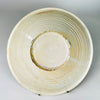 Reverse of an antique Spanish lebrillo bowl showing the cream glazed earthenware body, circular foot ring and pronounced concentric throwing ridges left by wheel construction. Irregular glaze pooling, kiln traces and age related surface wear document handmade manufacture, while the broad base confirms the piece was formed as a functional shallow basin.