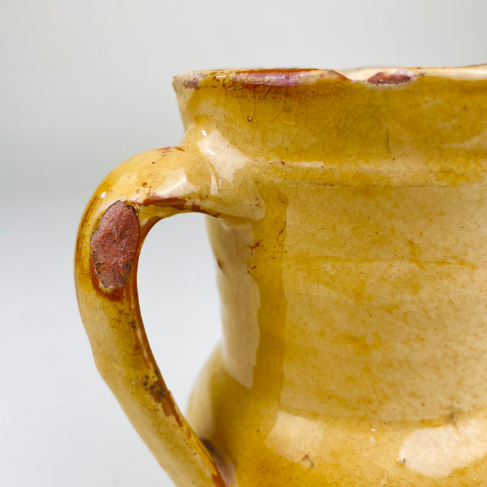 Spanish terracotta jug sourced in Peñafiel, Valladolid, measuring 15.5 cm high and 12 cm wide from spout to handle. Its wheel-thrown earthenware form carries a mottled yellow glaze over red clay, with a bulbous lower body, narrow waist and practical pouring lip characteristic of traditional Castilian folk pottery.