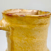 Yellow terracotta jug from Spain with a compact sculptural profile measuring 15.5 cm tall and 12 cm across the handle and spout. The antique pottery vessel has a bulbous body, upright neck, hand-formed lip and warm honey glaze, offering an authentic Mediterranean kitchen decor accent for shelves or collected ceramics.