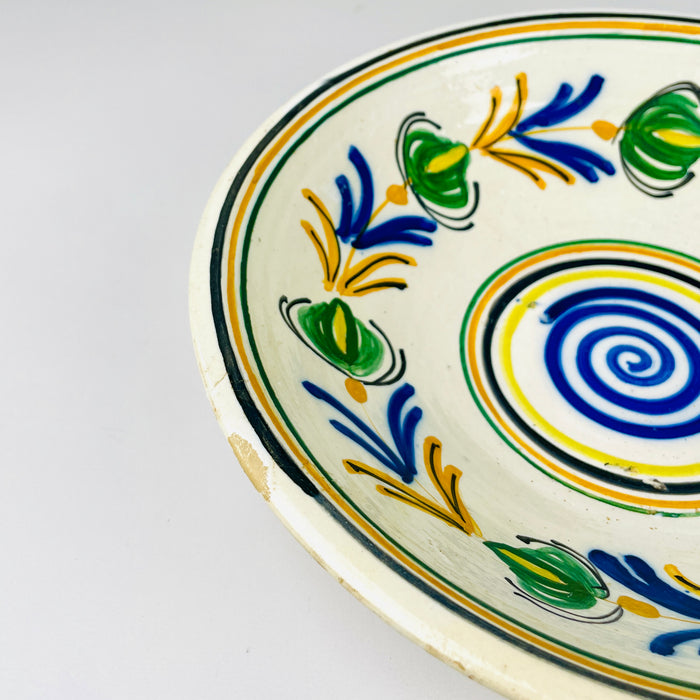 Antique Spanish lebrillo bowl identified by its 28.5 centimeter width, 7 centimeter height and 800 gram weight. The early 20th century glazed earthenware has a Castilian remolino arrangement of cobalt blue leaves, green flowers, yellow branches and black outlines around a spiral centre, useful as ceramic wall art or a shallow decorative basin.