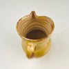 Rustic Spanish pottery jug with yellow earthenware glaze, a shaped pouring lip and a long handle attached at the neck and shoulder. The 19th century pitcher retains warm ochre color, irregular wheel marks, rim chips and glaze abrasions, providing substantial antique character for Mediterranean decor, farmhouse decor or vintage kitchen styling.