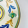 Castilian pottery decoration on an antique lebrillo bowl, with rounded green vegetal motifs edged in black and joined by fine ochre stems. Cobalt blue and honey yellow flourishes fill the spaces between them, while concentric border lines repeat the circular form. The lively palette complements cottage decor while remaining grounded in Spanish folk art.