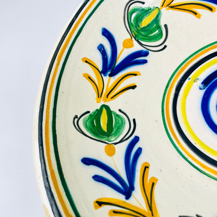 Hand painted Spanish lebrillo from the early 20th century, featuring a cream glazed ground, cobalt blue spiral centre and a continuous garland in green, yellow and black. The circular composition is easy to read from across a room, making this folk pottery bowl a strong focal point for eclectic decor, collected ceramics or a colorful plate wall.