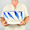 Expressive cobalt blue brushstroke on the exterior of the large Fajalauza lebrillo bowl, painted over a warm cream glaze with visible handmade texture and tiny firing pinholes. The flowing motif ends in a fine trailing line beneath the blue rim, illustrating the direct freehand decoration associated with this Los Arrayanes Granada pottery piece.