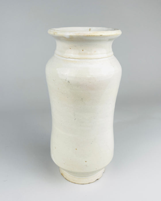Undecorated reverse of a vintage Spanish Talavera albarello jar, showing the smoothly glazed white earthenware, rounded shoulders, gently narrowed middle and small raised circular foot. The curved body is finished in an off-white glaze with scattered fine speckles and areas of subtle surface wear. The unpainted section highlights the traditional wheel thrown form of this pharmacy-style ceramic vessel.