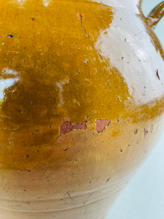 Provencal antique confit jar with ochre glaze drips and aged earthenware surface.