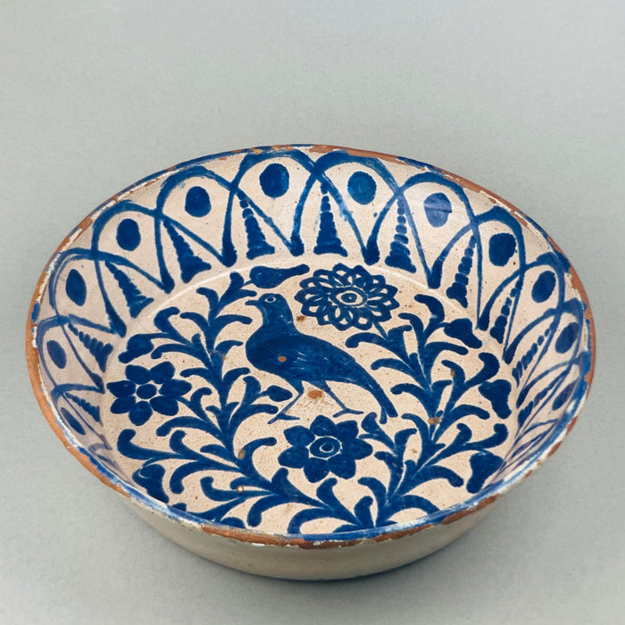 Top-down view of a large vintage Fajalauza ceramic bowl with bird motif and geometric Moorish scrollwork, radiating outward from the center in deep cobalt blue glaze on a softly aged white background, typical of Granada folk pottery.