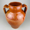 Full view of a large antique terracotta pot with two loop handles and a glossy brown slip glaze over red clay. The rounded shoulder and tapered lower body give it strong sculptural presence as vintage home decor, suitable as a decorative vase in French country decor or Mediterranean decor.