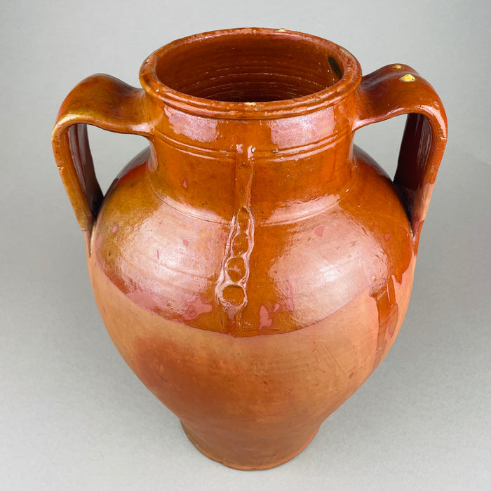 Full view of a large antique terracotta pot with two loop handles and a glossy brown slip glaze over red clay. The rounded shoulder and tapered lower body give it strong sculptural presence as vintage home decor, suitable as a decorative vase in French country decor or Mediterranean decor.