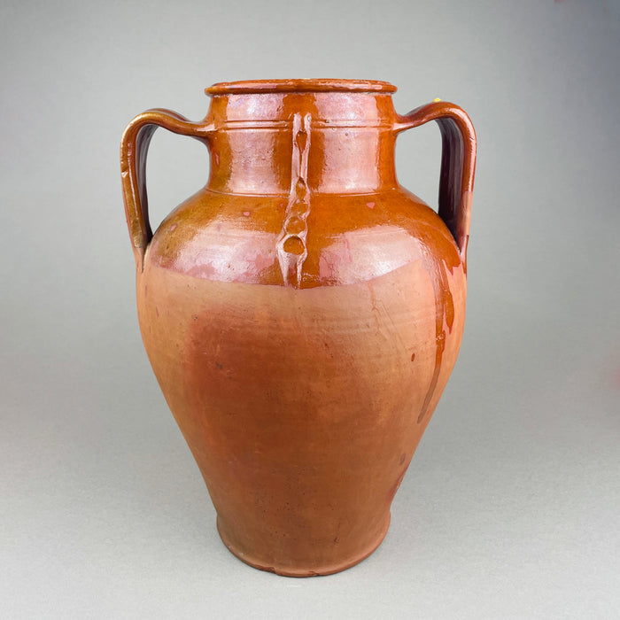 Antique terracotta decorative pot with twin handles, warm red clay body, and a glossy brown slip glaze that pools around the shoulder and neck. The ovoid form and wide mouth read as a decorative vase for vintage home decor, styled as farmhouse decor or French country decor with wood, linen, and natural tones.