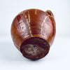 Base detail of an antique Spanish glazed terracotta orza jar, showing the flat circular foot, concentric wheel thrown lines and natural red clay surface. The utilitarian Castilian pottery construction supports its identity as a nineteenth century storage vessel, now suitable as a decorative vase for wabi sabi decor or rustic home decor.