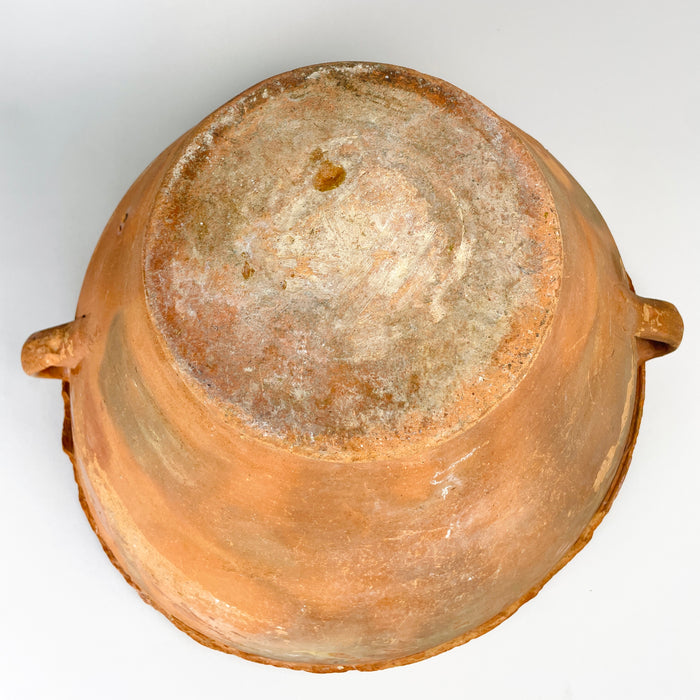 Antique Spanish pottery base showing concentric tool marks, surface abrasion and mineral discoloration across the unglazed terracotta. The broad foot is integral to the deep conical construction of the lebrillo bowl, which retains two side handles, a rolled rim and a warm glazed interior suitable for display as a rustic terracotta vase or centerpiece.