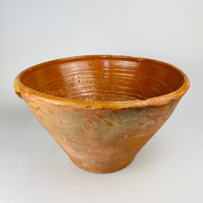 antique Spanish lebrillo bowl, formed from thick terracotta and joined beneath the broad rolled rim. The handle retains amber glaze, kiln speckling and wear from prolonged use, while the surrounding exterior shows layered patina, glaze drips and surface abrasion characteristic of an old working pottery vessel.